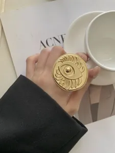 Close-up detail of vintage gold-plated statement eye ring, artistic retro design on hand.