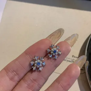 Close-up detail of sparkling snowflake stud earrings with blue stones and pearls.