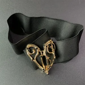 Detalle cercano del cinturon elastico negro con elegante hebilla de corazon dorado.