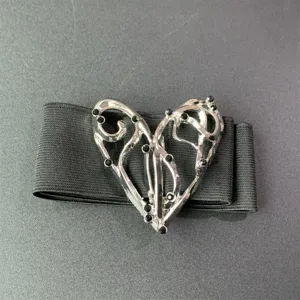 Primer plano de la hebilla de corazón de metal plateado con pedrería negra en el cinturón elástico.