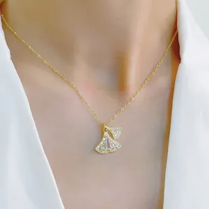Detail shot of sparkling zircon ginkgo leaf pendant necklace on neck, elegant gold-tone chain.
