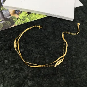 Gold layered anklet bracelet with delicate snake chain and feather charms detail shot.