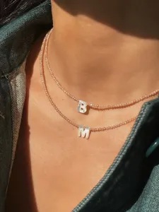 Nahaufnahme von zarten Perlen-Halsketten mit eleganten Muschel-Buchstabenanhängern.