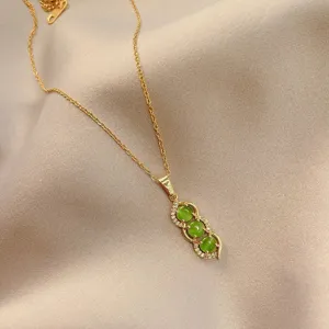 Close-up of gold chain necklace with triple green stone pea pod pendant and clear zirconia.