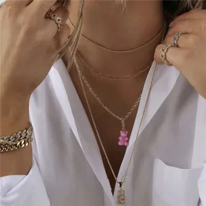 Vista detallada de collares dorados en capas con colgante de osito rosa, joyería.