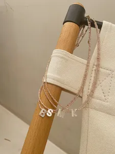 Detailaufnahme einer zarten Perlen-Choker-Kette mit glänzenden Muschel-Buchstaben.