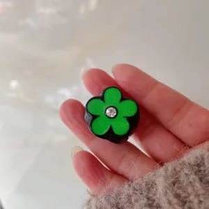 Close-up detail of a chic black and green five-petal flower ring with a sparkling rhinestone center.