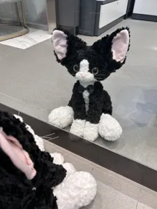 Detailed close-up shot of the black and white curly plush cat toy with elegant bow tie.