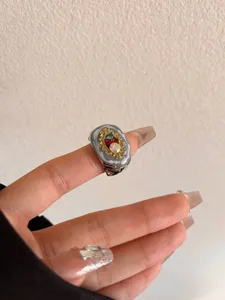 Close-up van brede retro metalen ring met kleurrijke strass-stenen en oliedruppeldetails op vinger.