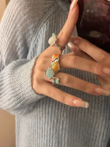 Close-up detail of multi-layered gemstone rings featuring natural colorful stones and irregular metal.