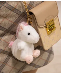 Gros plan d'un mignon pendentif porte-clés licorne en peluche blanche sur sac beige.