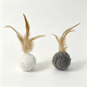 Close-up detail shot of fuzzy cat toy balls with natural feathers in white and grey.