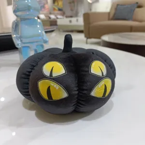 Vue détaillée de la peluche citrouille d'Halloween noire avec des yeux de chat jaunes vibrants.