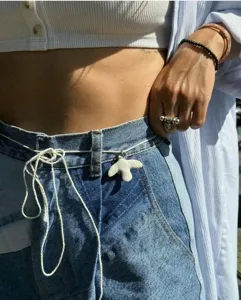 Close-up detail of white ceramic dove pendant worn as stylish waist chain accessory on denim.