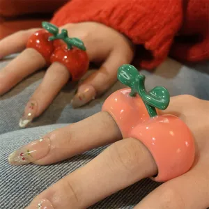 Gedetailleerd overzicht van emaille kersen en perzik fruit ringen, trendy statement sieraden.