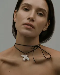 Close up detail of a white ceramic dove pendant on a black cord choker necklace, elegant style.