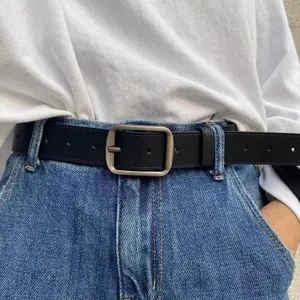 Close-up of minimalist black leather belt with retro metal pin buckle for casual denim jeans.