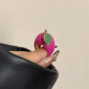 Detailfoto van een opvallende roze emaille fruitring met groen blad, stijlvol sieraad.
