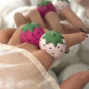Close-up detail van schattige grove aardbei emaille ringen, zoete macaron stijl statement sieraden.