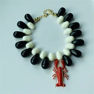Collier ras du cou tendance avec pendentif homard et perles en résine noire et blanche.