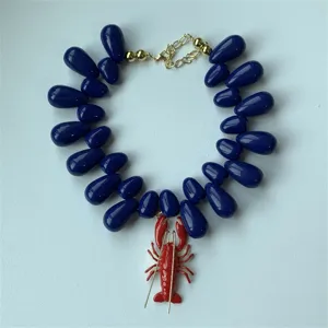 Collier pendentif homard tendance avec perles en résine bleu foncé et chaîne dorée.