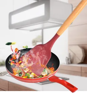 Silicone cooking spatula with wooden handle in frying pan detail view for kitchen use.