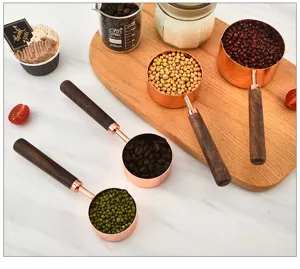 Stainless steel measuring cups and spoons set with walnut wood handles in rose gold finish detail view.
