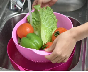 Kitchen draining basket detail shot, pink plastic double-layer colander washing fresh vegetables in sink.
