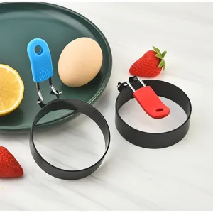 Stainless steel fried egg mold detail view with colorful silicone handles and kitchen props.