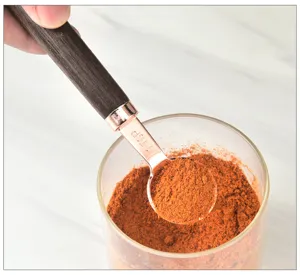 Close-up detail view of the rose gold measuring spoon scooping red spice powder easily.