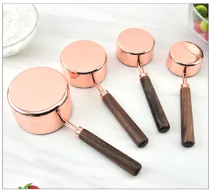 Rose gold measuring cups set with walnut wood handles for kitchen baking and cooking use.