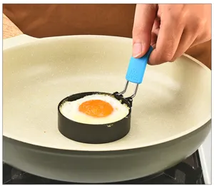 Close-up detail of the black stainless steel round fried egg mold in use during cooking.