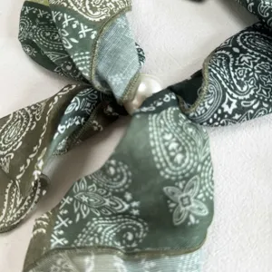 Close-up detail of green paisley silk scarf featuring an elegant central pearl accessory.