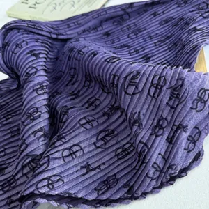 Close-up detail of a purple pleated fabric scarf featuring elegant dark monogram pattern.