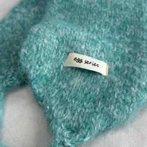 Gemütliche türkisblaue Strick-Ohrenklappenmütze mit Bändern und Stoffetikett für den Winter.
