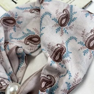 Close-up detail of vintage paisley patterned small silk scarf with pearl charm accessory.