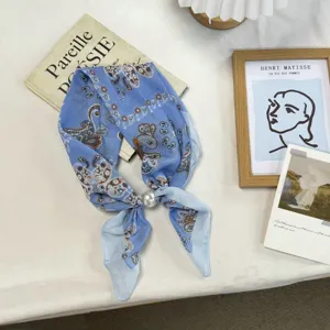 Detailed shot of light blue paisley pattern small silk scarf with pearl ring decor flat lay.