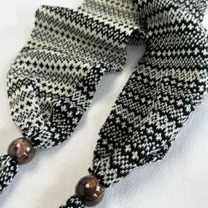 Vista detallada de la bufanda estrecha de punto blanco y negro con borlas de cuentas.