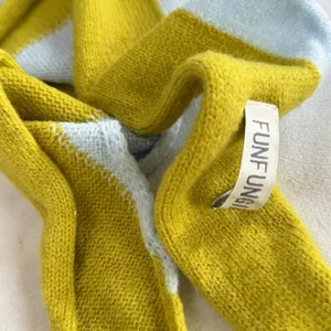 Close-up detail of a color-blocked knitted scarf in yellow and blue, showing soft wool texture.