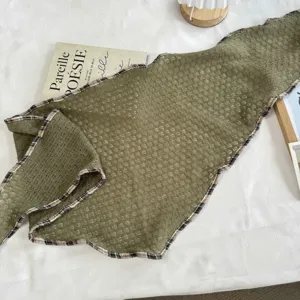 Detalle del pañuelo triangular calado de punto verde oliva con borde de cuadros clásico.