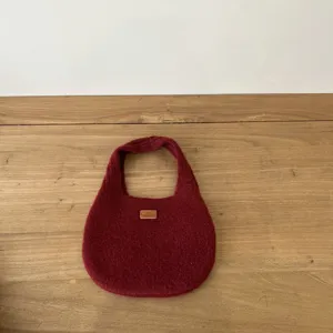 Closeup of the dark red knitted handbag featuring a handmade leather tag and soft wool texture.