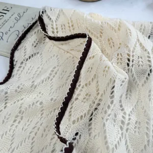 Close-up detail of cream knitted lace scarf with dark brown trim, hollow-out texture design.