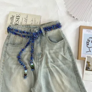 Detailweergave van light-wash jeans met een unieke pluizige blauwe gevlochten riem met kralen.