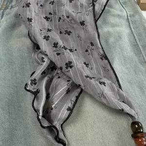 Detailed view of a chic grey floral triangular scarf featuring delicate wooden bead pendants.