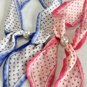 Closeup detail of narrow printed silk scarf with polka dots, bows and elegant pearl buckle.