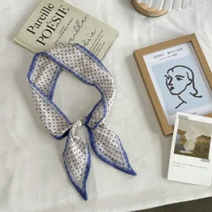 Detail view of a chic narrow long twilly scarf with blue polka dots and a pearl buckle.