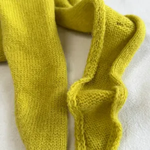 Close-up detail of green knitted scarf texture showing soft fabric and fine knit pattern.