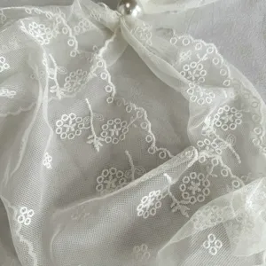 Close-up detail view of white lace mesh scarf with elegant floral embroidery and pearl.