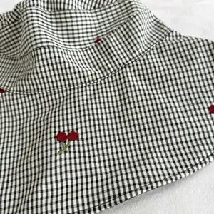 Detailed view of fashionable black and white gingham sun hat with embroidered red cherry motifs.