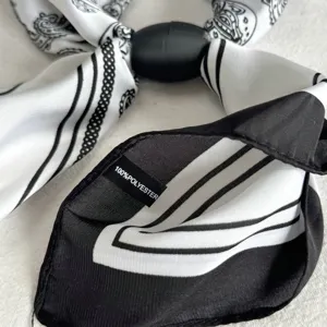 Close-up detail of black and white printed neck scarf with black ring and polyester tag.